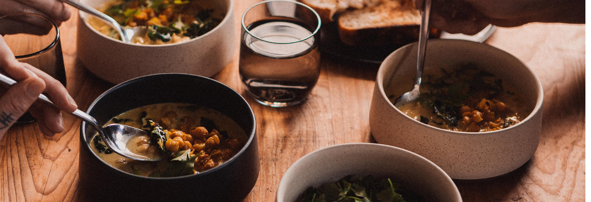 A close up dinner scene focusing on 4 ceramic bowls as spoons enter a chickpea like stew or curry.
