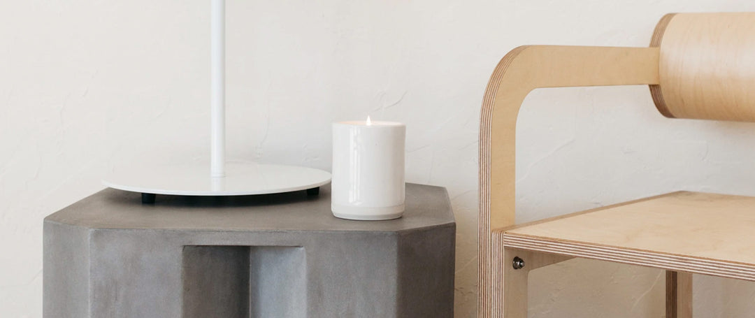 A white ceramic candle on top of a cement side table.