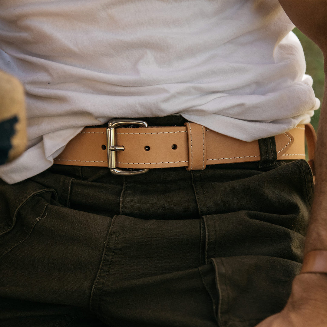 Close in shot of a torso wearing a natural colored leather belt with accent stitching and stainless buckle.