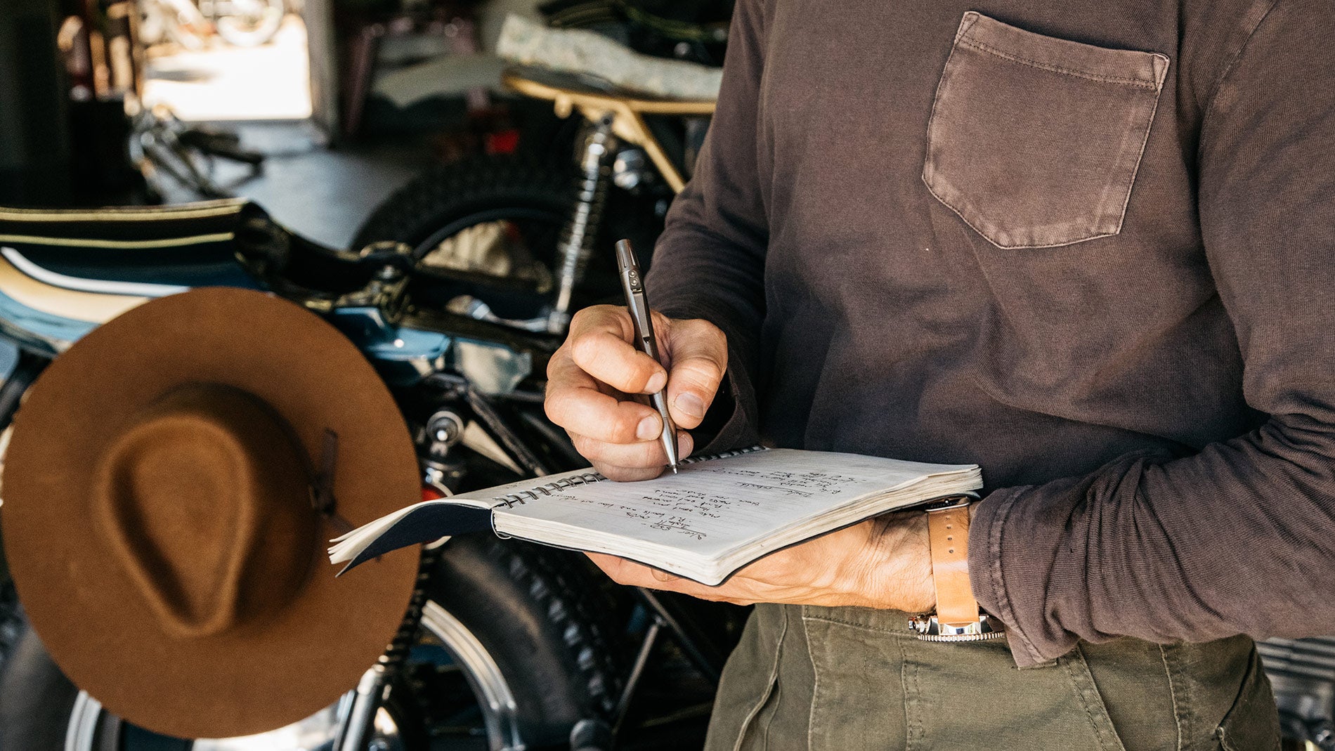 A man inside his motorcycle garage, writing in his journal with a Tanner Goods titanium Memori pen.