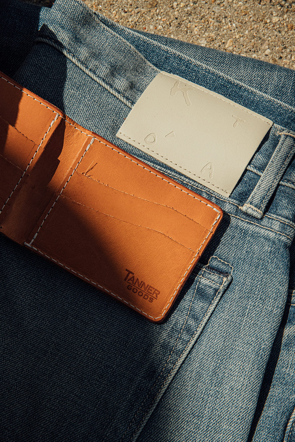 An open Tanner Goods Bifold laying on the back of a pair of KATO light colored denim.