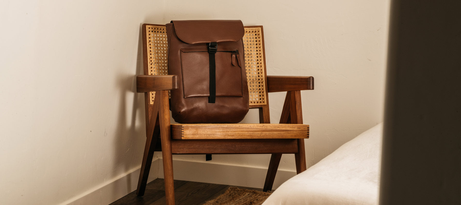 An all leather backpack resting on a wooden chair in a bedroom.