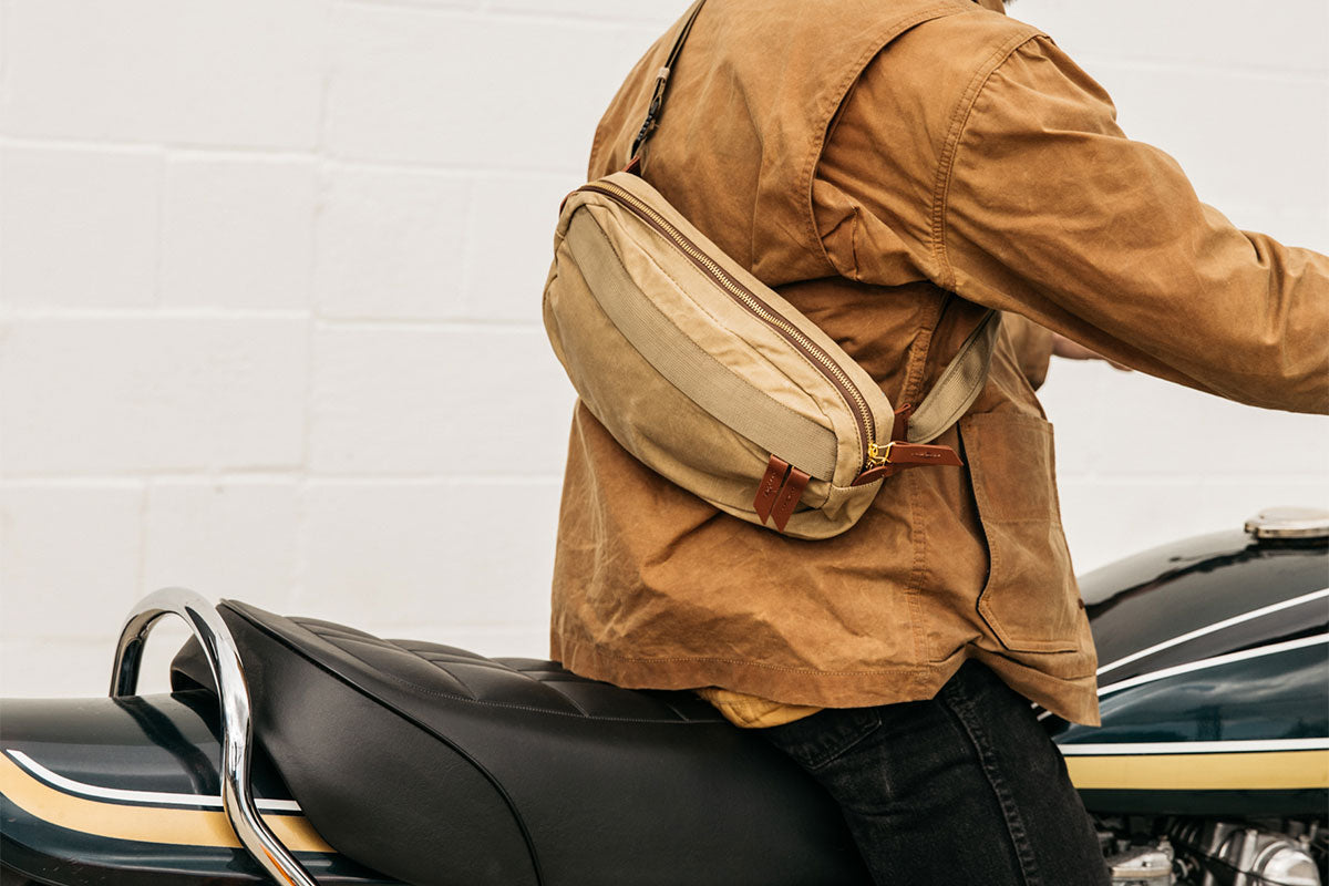 Person wearing a utility tan crossbody sitting on a motorcycle. 