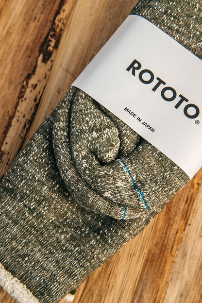 Army green double face crew socks with a speckled knit texture, blue stripe, folded on a wooden surface.