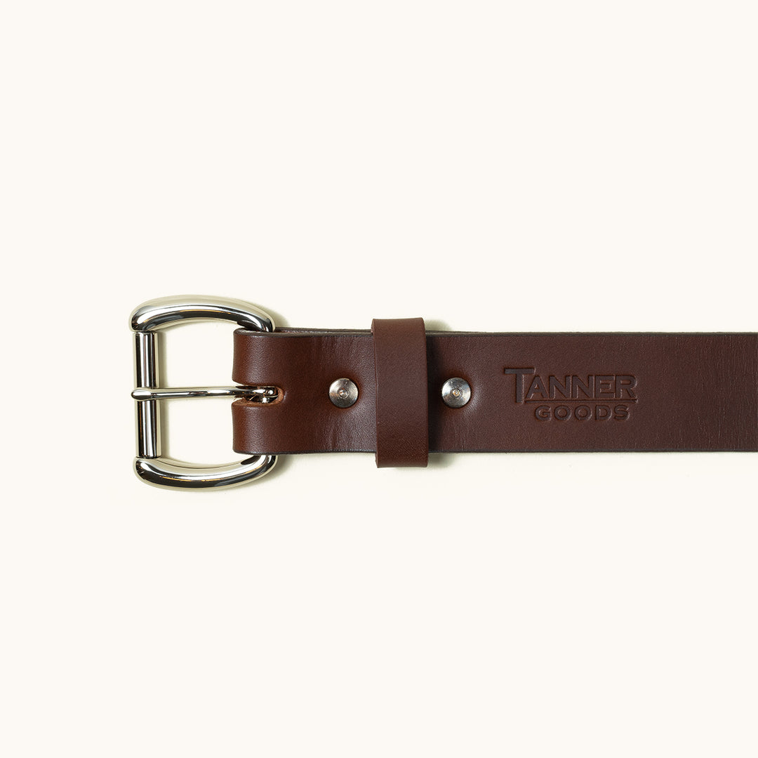 The top half of a Cognac Standard belt showing a stainless roller ball buckle and Tanner Goods logo stamped into the belt.