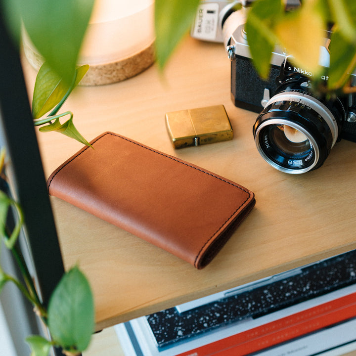 An Aspect Bifold laying on a desk next to a gold lighter and slr camera.