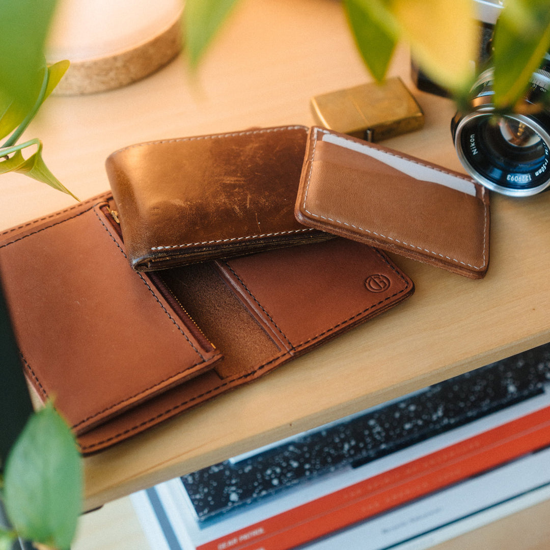 An Aspect Bifold, Journeyman, and used Bifold showing a patina, laying on a desk next to a gold lighter and slr camera.