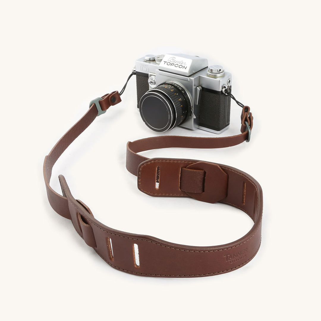 A silver and black SLR camera with a cognac leather strap.