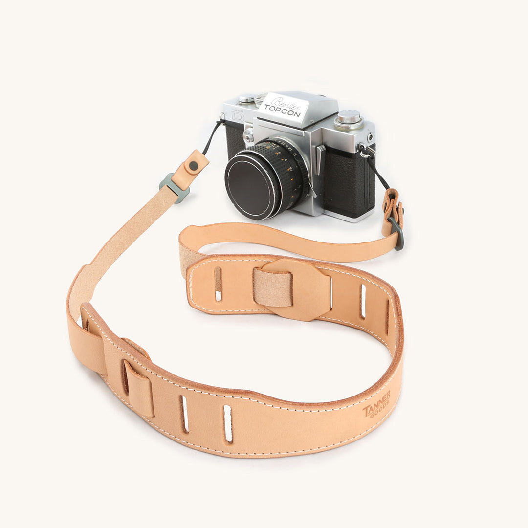 A silver and black SLR camera with a natural leather strap.