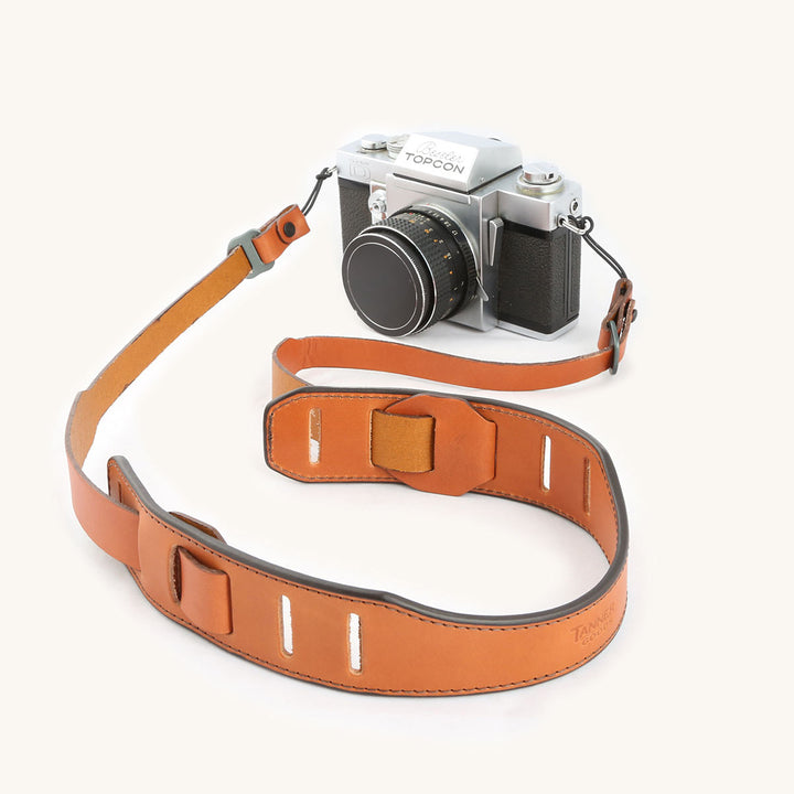A silver and black SLR camera with a saddle-tan leather strap.