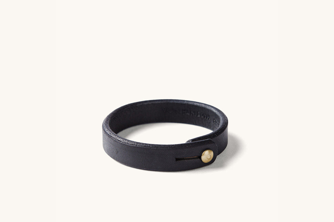A black leather wristband with brass rivet closure.