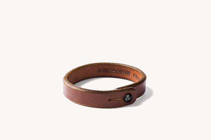Brown leather wristband with a black rivet closure.