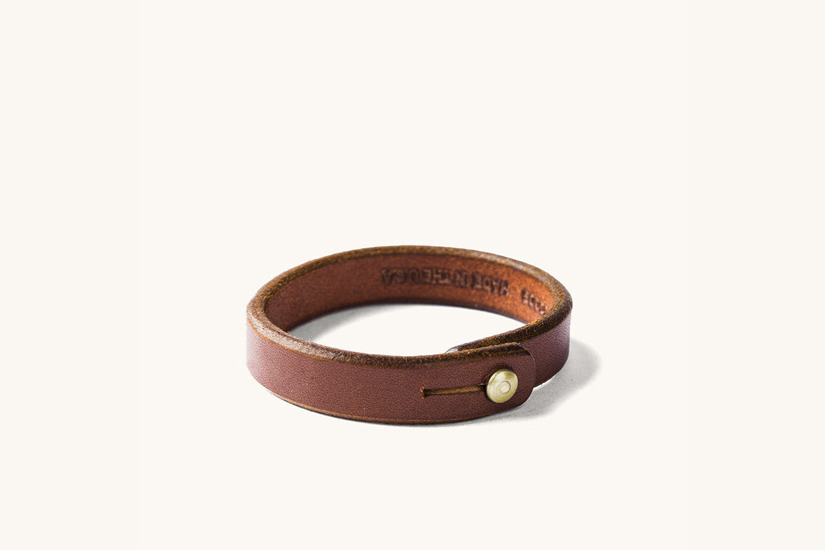 Brown leather wristband with brass rivet closure.