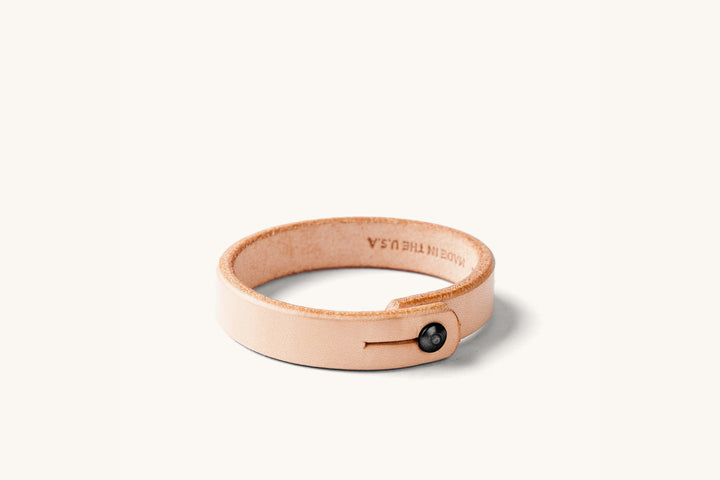 Small natural leather wristband with black rivet closure and "Made in the USA" monogram on the underside.