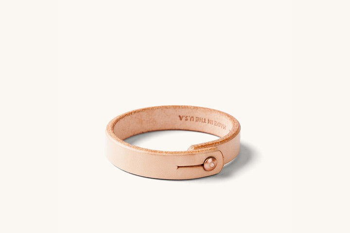 Small natural leather wristband with copper rivet closure and "Made in the USA" monogram on the underside.