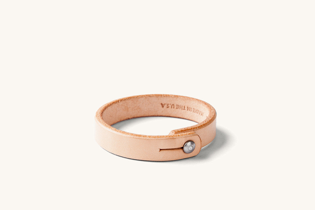 Small natural leather wristband with rivet closure and "Made in the USA" monogram on the underside.