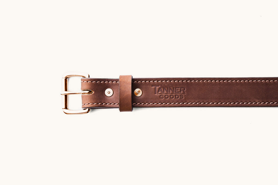 the front half of a brown leather belt with copper roller buckle and Tanner Goods monogram