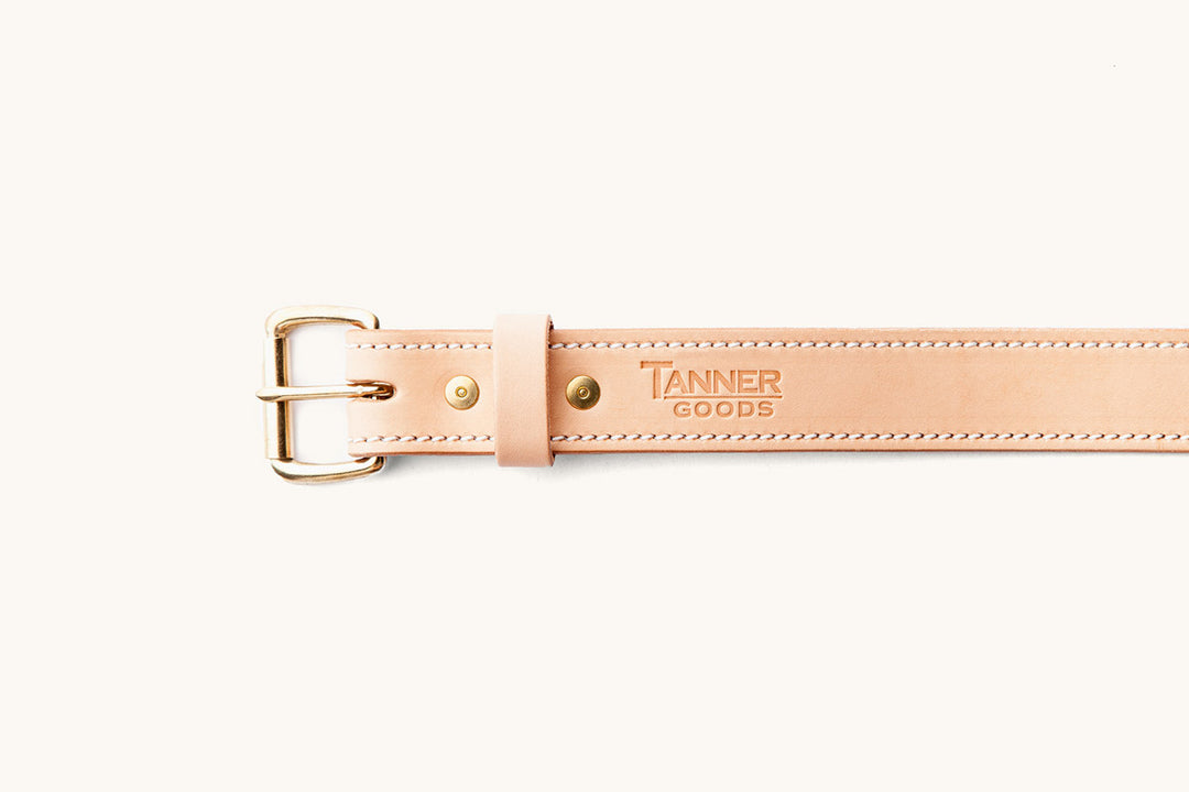 the front half of a sand colored belt with brass hardware and a Tanner Goods monogram