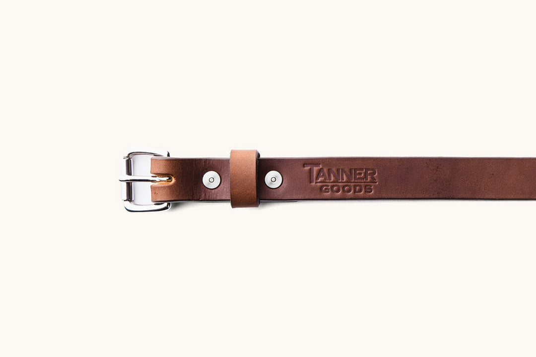 the first half of a brown leather belt with silver hardware and a Tanner Goods logo monogram
