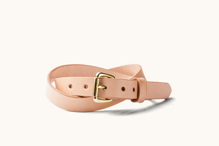 a narrow, sand colored leather belt with a brass roller ball buckle