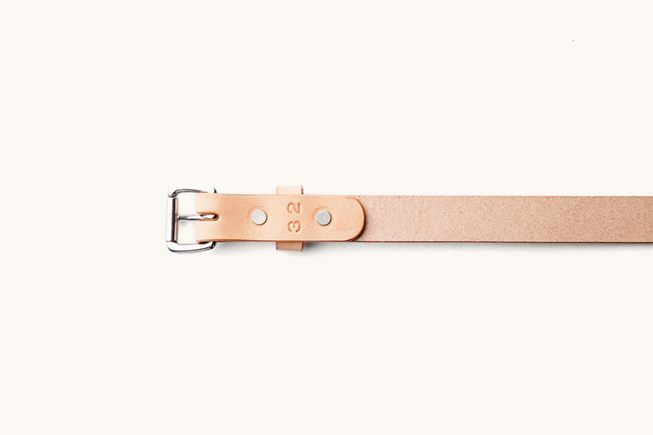 the rough leather underside of a sand colored leather belt with silver hardware